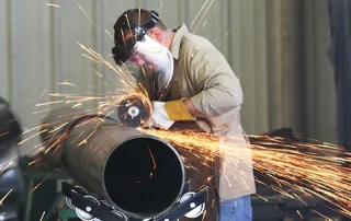 Mechanical contractor using a grinder on a steel pipe in a fabrication shop