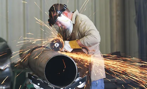 Mechanical contractor using a grinder on a steel pipe in a fabrication shop